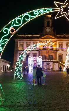 two people standing under an arch decorated with christmas lights in front of a large building