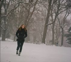 a woman is walking through the snow with trees in the background