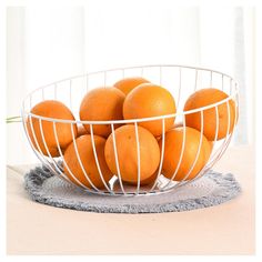 a white wire bowl filled with oranges on top of a table