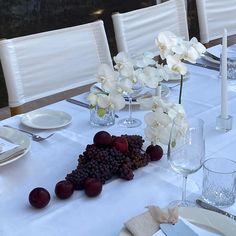 the table is set with white flowers, grapes and wine glasses for an elegant dinner