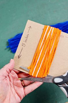 a pair of scissors is being used to cut orange thread on a piece of cardboard