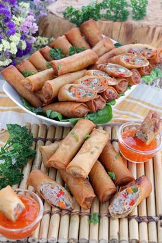 there are many appetizers on the table with dipping sauces and flowers in the background