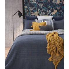 a bed with blue and yellow comforters, pillows and blankets on top of it