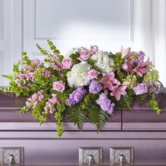 a purple casket with flowers and greenery on it's side, in front of a white door