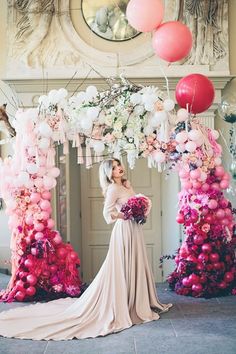 a woman standing in front of balloons and flowers on display at a wedding reception with pink, white and red decorations