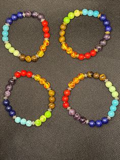 four bracelets with different colored beads on a gray surface and one has an orange, yellow, green, blue, and red bead