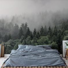 a bed sitting in front of a forest wallpapered with foggy trees and mountains