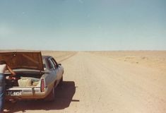 a man standing in the back of a pick up truck on a dirt road with his trunk open