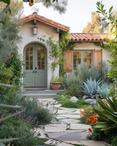 a house that is surrounded by plants and flowers in front of the entrance to it