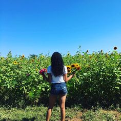 a woman standing in front of a field of sunflowers with her back to the camera