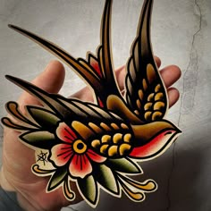 a hand holding a bird with flowers painted on it's body and wings flying in the air