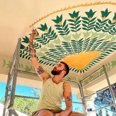 a man sitting on top of a stepladder painting a mural onto the ceiling