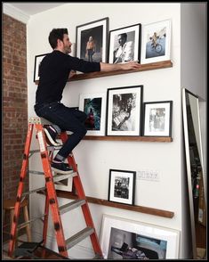 a man sitting on top of a ladder next to a wall filled with framed pictures