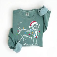 Wrap yourself in holiday cheer with our Festive Pitbull Christmas Sweatshirt! This cozy pullover showcases a cheerful Pittie wearing a Santa hat and wrapped in colorful Christmas lights, bringing warmth and joy to chilly winter days. The soft, green fabric is perfect for snuggling up by the fire or taking your loyal companion for a holiday walk. It's an ideal gift for Pitbull fans, dog moms, or dads who appreciate a touch of whimsy with their loving four-legged friends. Whether you're decorating Dog Christmas Sweater, Xmas Gifts For Mom, Gsp Dogs, Christmas Attire, Christmas Gifts For Parents, Pointer Dog, Pitbull Mom, Funny Christmas Sweaters, Dog Christmas Gifts