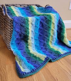 a crocheted blanket sitting on top of a wooden floor next to a basket