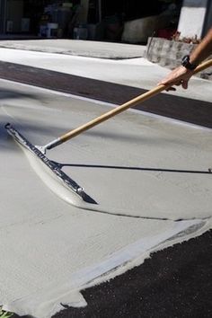 a man is using a broom to clean the cement from the sidewalk in front of his house