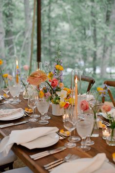 the table is set with flowers, candles and place settings for an outdoor dinner party