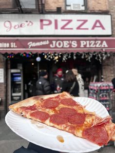 a slice of pepperoni pizza on a paper plate in front of a storefront