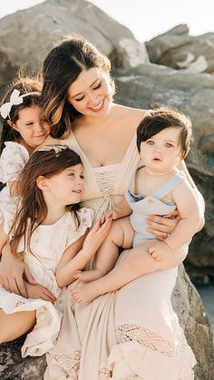 a woman is holding two small children and posing for the camera with her three other girls