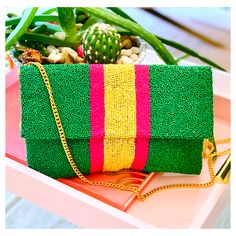 a green and pink clutch bag sitting on top of a table next to a cactus