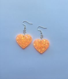 "Each pair of resin earrings are handmade to order, therefore no two pairs are identical! Each item is slightly unique and one of a kind. However, I try to get as close as possible :) Made with nickel free, hypoallergenic, sterling silver fish hooks.  Heart width is approximately 1.25\", and is made with epoxy resin, orange glow pigment, and chunky iridescent glitter with stars ✨ These neon orange heart earrings glow in the dark AND are ultraviolet blacklight reactive! Perfect for raves, parties Handmade Heart-shaped Resin Earrings, Heart-shaped Resin Earrings For Party, Orange Resin Jewelry For Party, Heart Shaped Resin Jewelry For Party, Glow Heart, Neon Earrings, Rave Jewelry, Orange Glow, Orange Heart