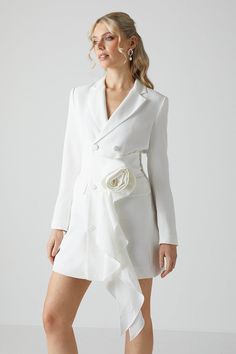 a woman in a white dress and jacket with flowers on the lapel is posing