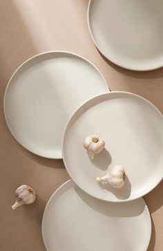 three white plates sitting on top of a table next to two garlic cloves