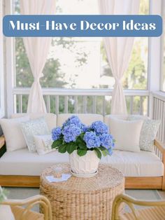 a living room with white furniture and blue flowers on the coffee table in front of it