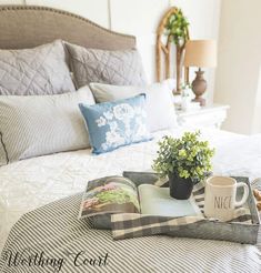 a tray with books, coffee mug and flowers on top of a bed in a bedroom