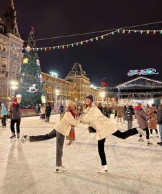 two people skating on an ice rink in front of a lit up christmas tree at night