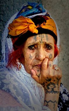 an old woman with tattoos on her face and hands in front of her face is looking at the camera