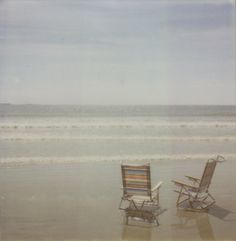 two lawn chairs sitting on top of a beach next to the ocean