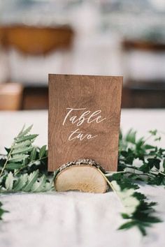 a wooden table with greenery around it and a place card holder on the top