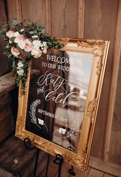 a sign with flowers and greenery on it sitting in front of a wooden wall