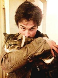 a man holding a cat in his arms while wearing a leather jacket and looking at the camera