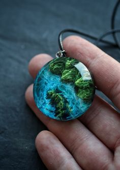 a hand holding a glass pendant with green leaves in the middle and blue water on it