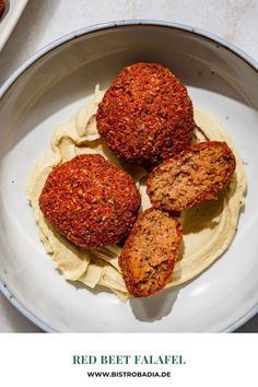 three meat patties on top of hummus in a white bowl with the words red beet falafel