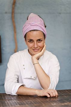 a woman sitting at a table with a pink towel on her head and smiling for the camera