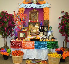 an altar with fruit and flowers on the table, surrounded by potted trees in front of it