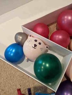 an assortment of balloons in a box with a cat face on one of the balloons