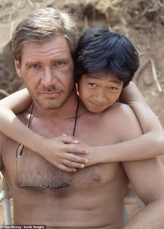 a shirtless man holding a young boy in his arms and looking at the camera