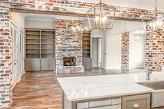 an empty kitchen and living room with exposed brick walls, white counter tops and wooden flooring