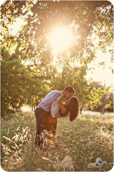 a man and woman kissing in the middle of a field with sun shining through trees