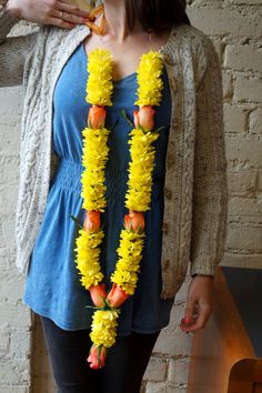 a woman standing next to a brick wall wearing a yellow lei with flowers on it