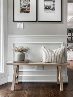 two framed pictures hang on the wall above a bench in a room with wood floors