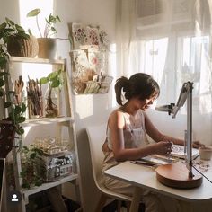 a woman sitting at a table working on a project with a lamp in front of her