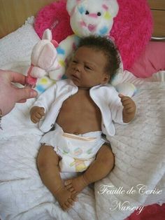 a baby is sitting on a bed next to a pink teddy bear and stuffed animal