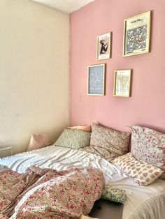 an unmade bed in a bedroom with pink walls and pictures on the wall above it