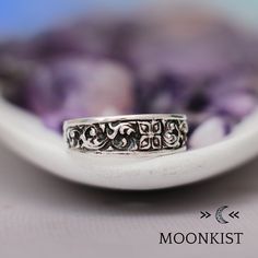 a silver ring sitting on top of a white plate with purple flowers in the background