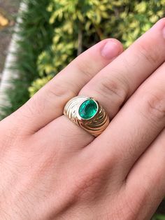 a person's hand wearing a gold ring with a green stone in the middle